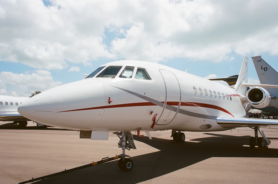 A white private jet with red stripes is parked on an airport tarmac under a partly cloudy sky, ready for private jet journeys to remote destinations.