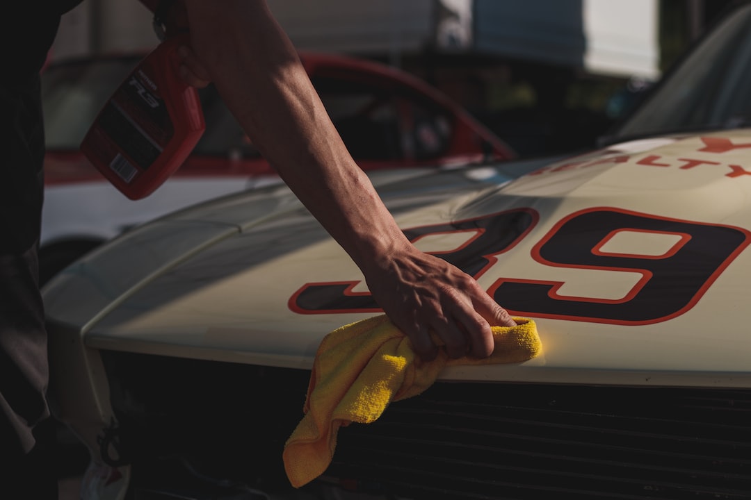 A person wipes the hood of a cream-colored racing car with a yellow cloth. The car has the number 39 painted in red and black.