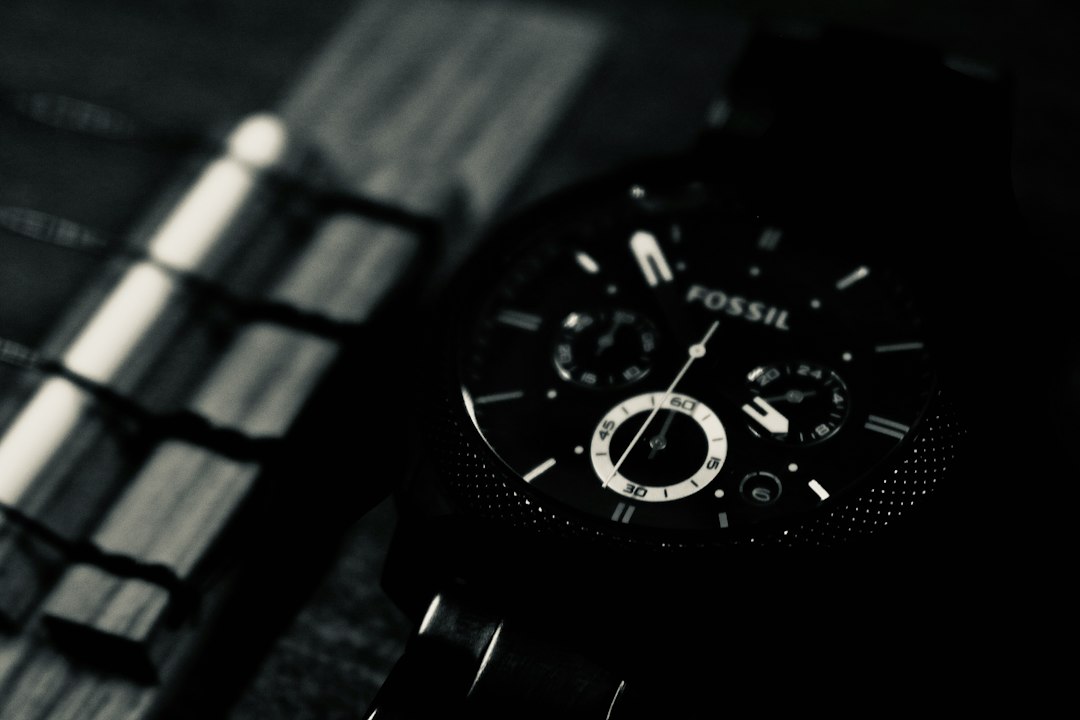 Close-up, black-and-white photo of a Fossil chronograph wristwatch with visible dials and hour markers, placed next to a wooden object with metal accents.
