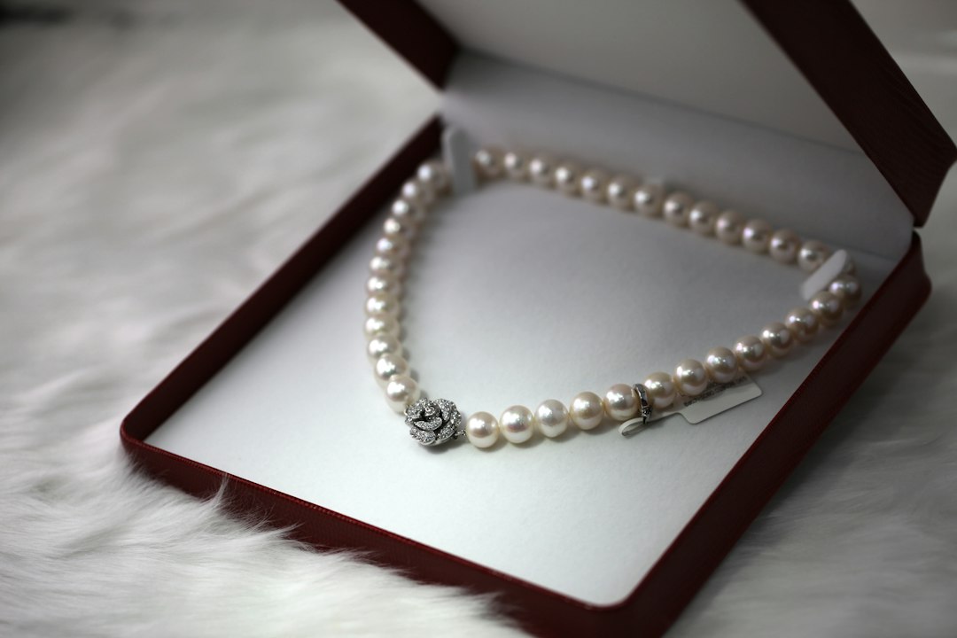 A pearl necklace with a decorative clasp, a must-have accessory for any collection, is displayed in an open red box lined with white fabric.