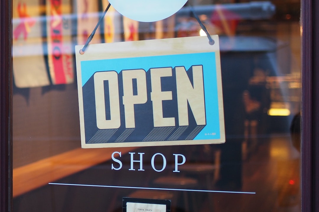 A blue and yellow "OPEN" sign hangs on a glass door above the word "SHOP," inviting you to buy jewelry online as the store is open for business.