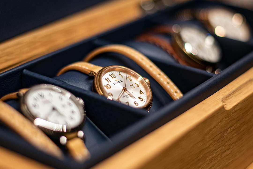 A close-up of several wristwatches with leather straps displayed in a wooden and navy blue watch box, perfect for those interested in investing in jewelry or seeking the finest luxury jewelry pieces.