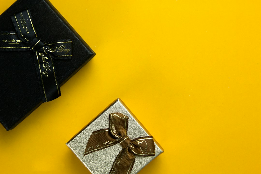 Two gift boxes with ribbons, one black and one silver, are placed on a yellow background—perfect inspiration for luxury gifts when spoiling your loved ones.