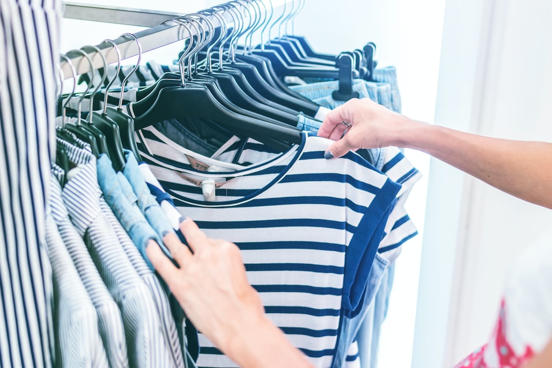 A person browsing and holding up a striped shirt on a clothing rack filled with luxury kids clothing, with multiple striped garments hanging on black hangers.