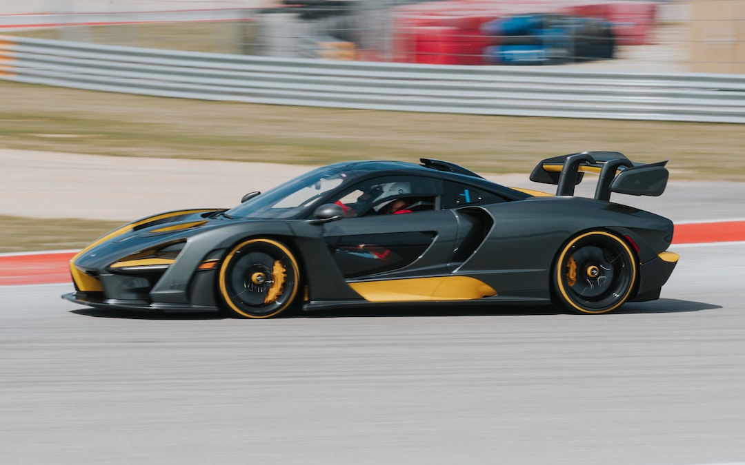A black and yellow sports car is driving on a racetrack with a blurred background, capturing the excitement of luxury sports car racing.