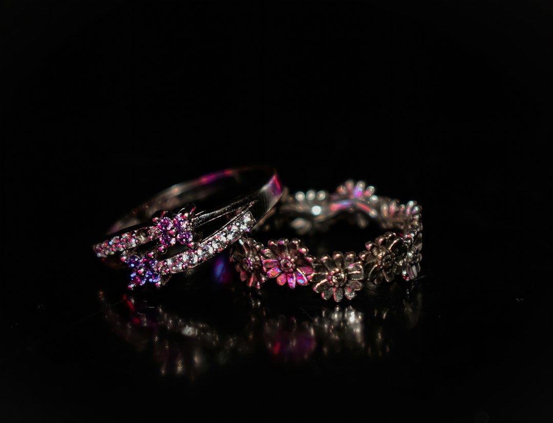 Two rings on a black background; one showcases pink gemstones, while the other features a floral design with small clear stones—capturing the timeless elegance of vintage jewelry.
