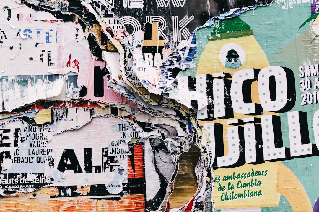 Close-up of a wall covered in layered, partially torn posters and advertisements for exclusive art exhibitions, with overlapping colors, text, and graphics.