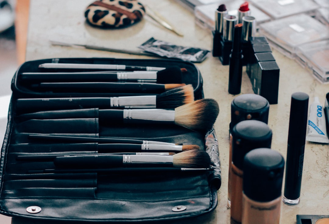 A set of makeup brushes in a black case, surrounded by lipstick, foundation bottles, a compact mirror, and other top beauty gadgets for achieving flawless skin on your vanity table.
