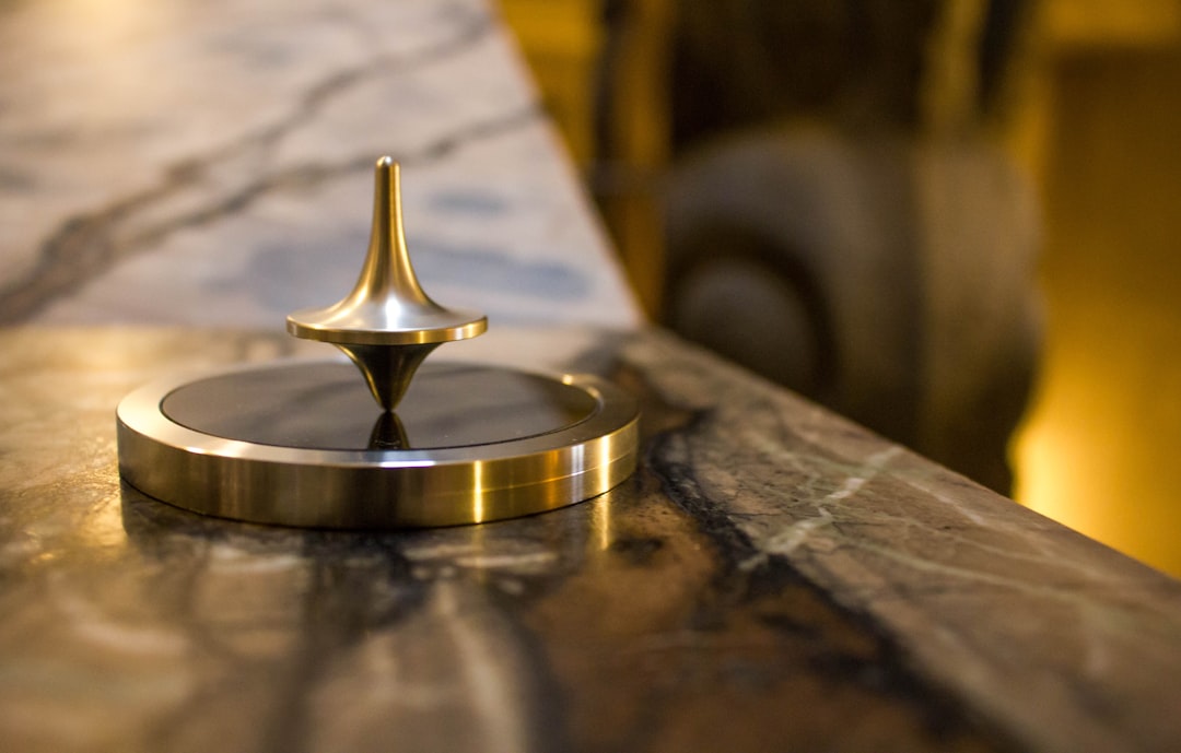 A brass spinning top is balanced upright on a black and gold circular base, evoking the elegance of luxury travel as it rests on a polished marble surface.