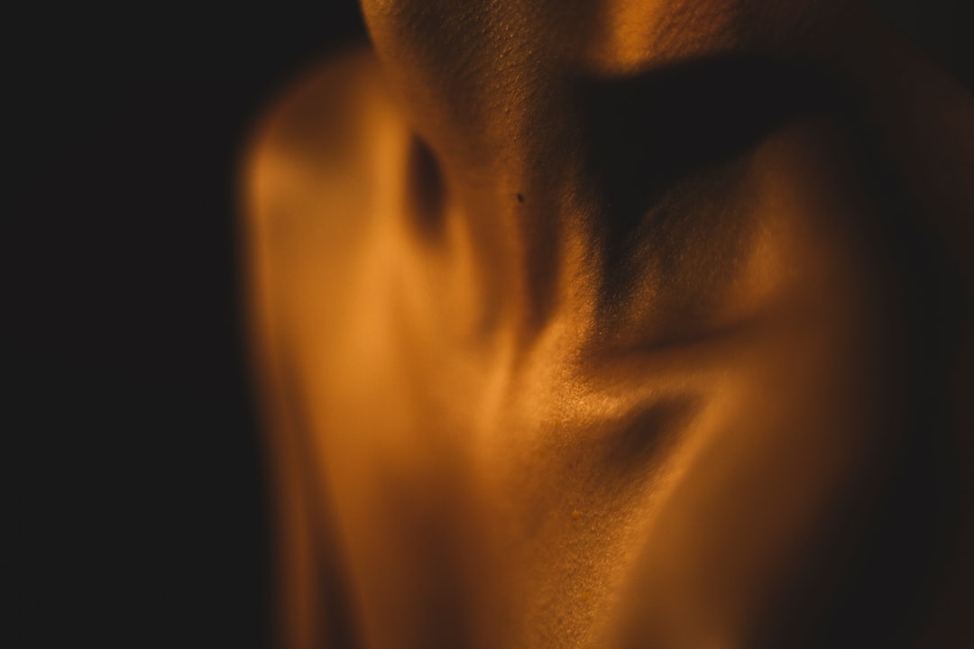 Close-up of a person's bare shoulders and neck in warm, low lighting, highlighting the contours and texture of the skin—an ideal way to showcase how primers work for every skin type.