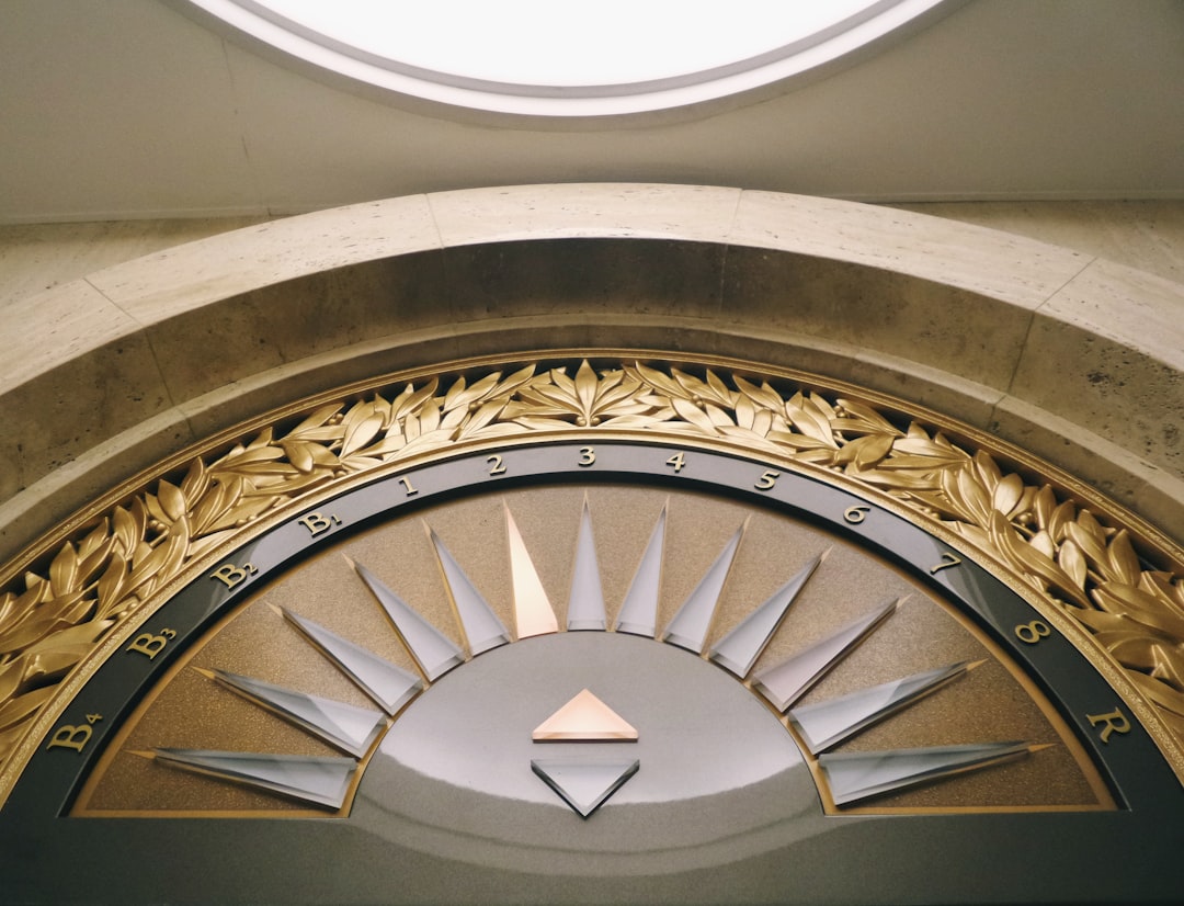 Decorative, semicircular elevator floor indicator panel with gold and silver accents, numbered 1 to 8, evokes the elegance of luxury travel, set into a stone arch under a round skylight.