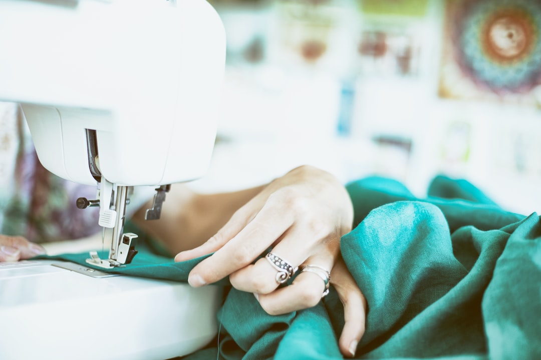 A person guides green fabric through a sewing machine, exploring each stitch with the precision and elegance of crafting designer jewelry.