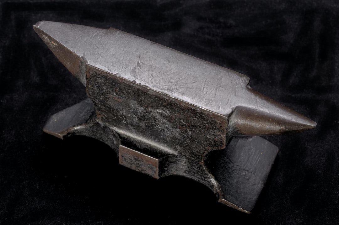 A metal anvil with pointed ends is placed on a dark, textured surface, ready to spark inspiration at any creativity workshop.