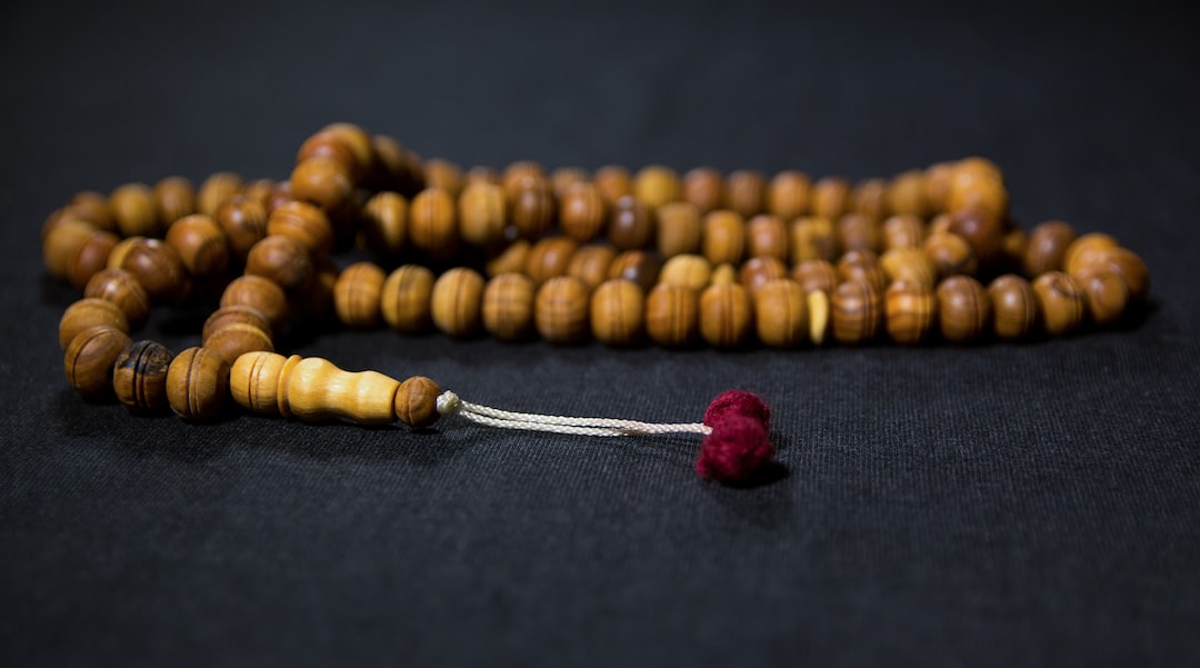 A wooden prayer bead mala with a red tassel rests on a dark surface, an elegant piece that beautifully bridges spirituality and jewelry.