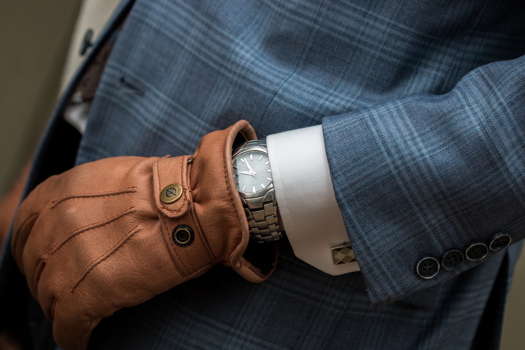 A person in a blue plaid suit and brown leather gloves displays a silver wristwatch on their left wrist, showcasing impeccable style with this elegant accessory.