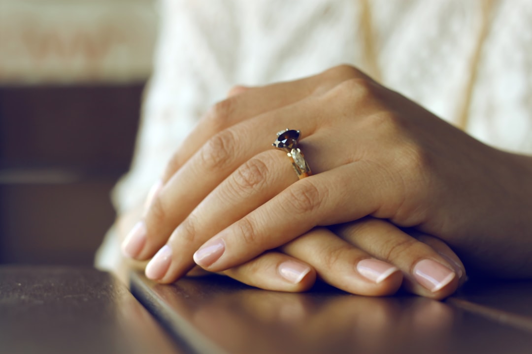 Close-up of a person's hands resting on a table, wearing cruelty-free nail polish and a gold ring with a dark gemstone on the ring finger.