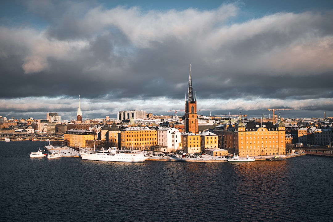 Aerial view of a waterfront cityscape with historic buildings, a tall church spire, boats docked along the shore, and dramatic clouds in the sky—perfect for exclusive tours and unforgettable waterfront experiences.