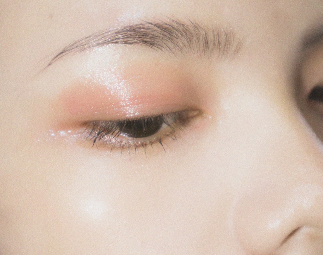 Close-up of a person's closed eye with glossy peach eyeshadow and defined eyebrow, highlighting smooth skin texture—an inspiring look for those seeking zero waste beauty in their greener routine.