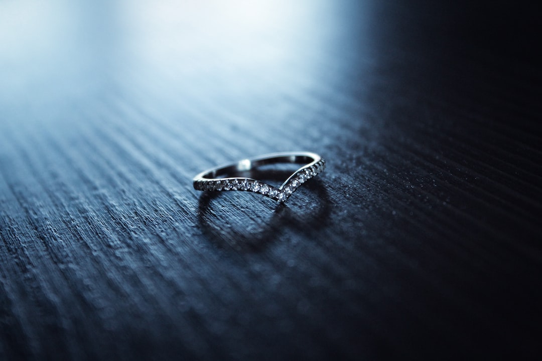 A silver ring with small diamonds arranged in a V shape, echoing diamond tradition, sits on a dark wooden surface.